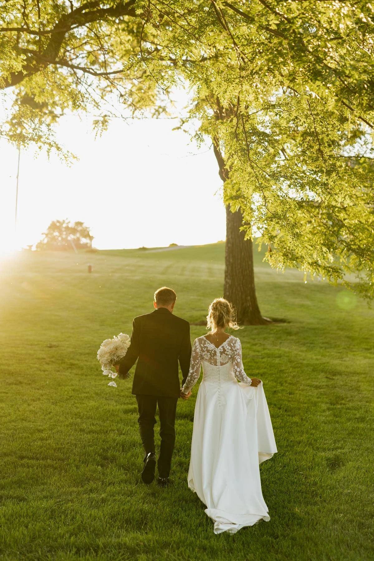 Bride and groom walking across the lawn under a shade tree