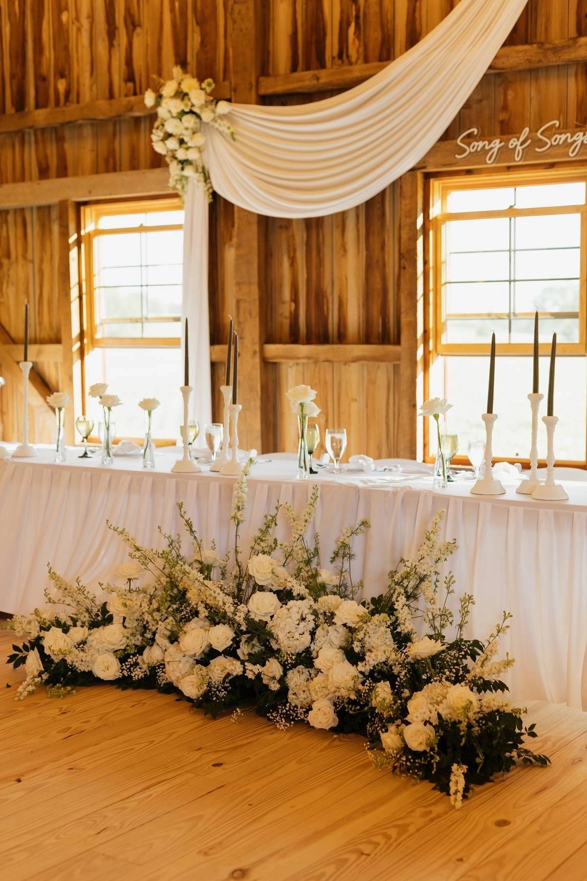 Sweetheart table with cascading white florals and candlelight inside the event barn