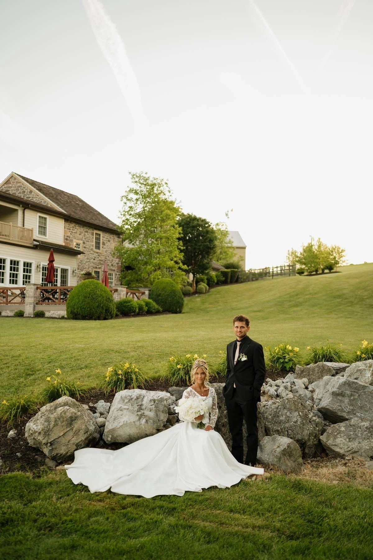 Bride seated on the rocks with her groom, wedding portrait on the property