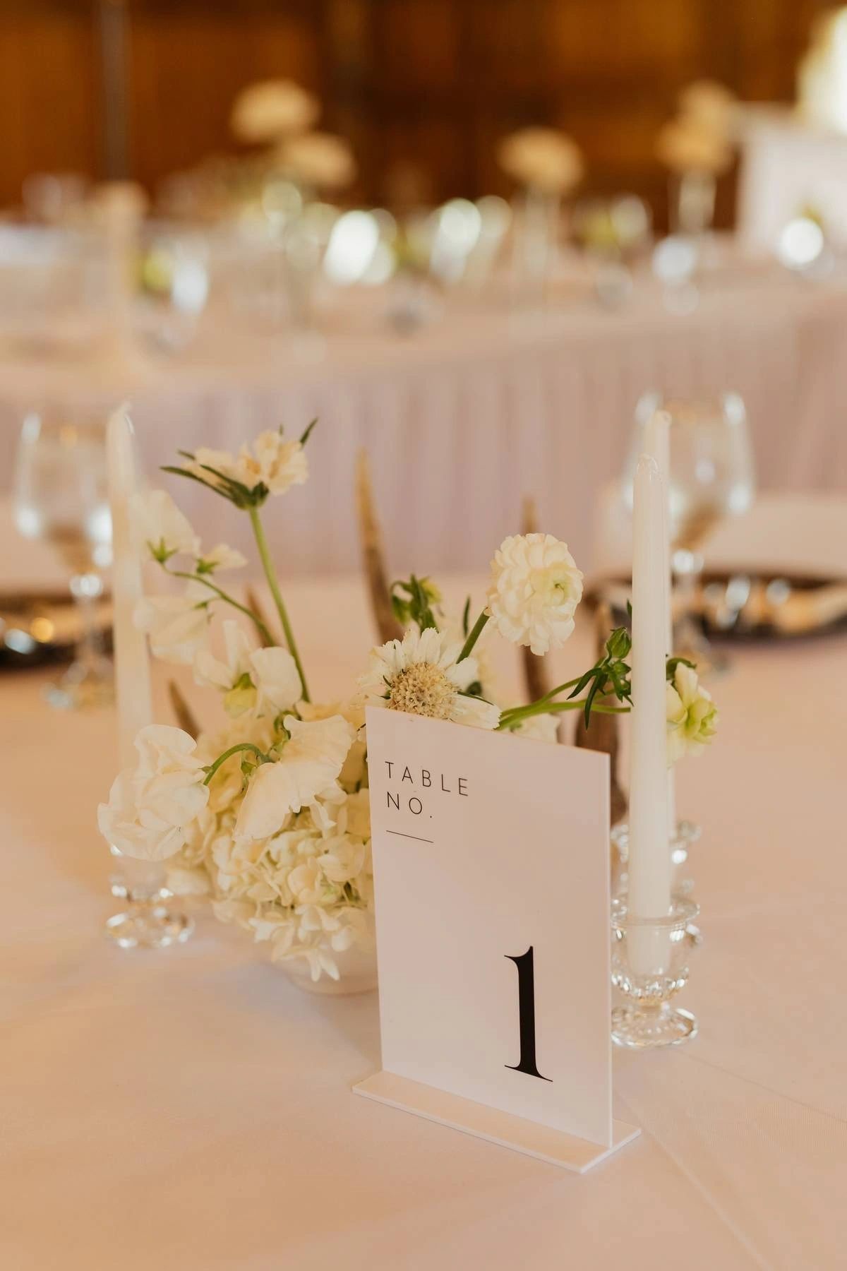 Close-up of a reception table number with white candles and floral centerpiece