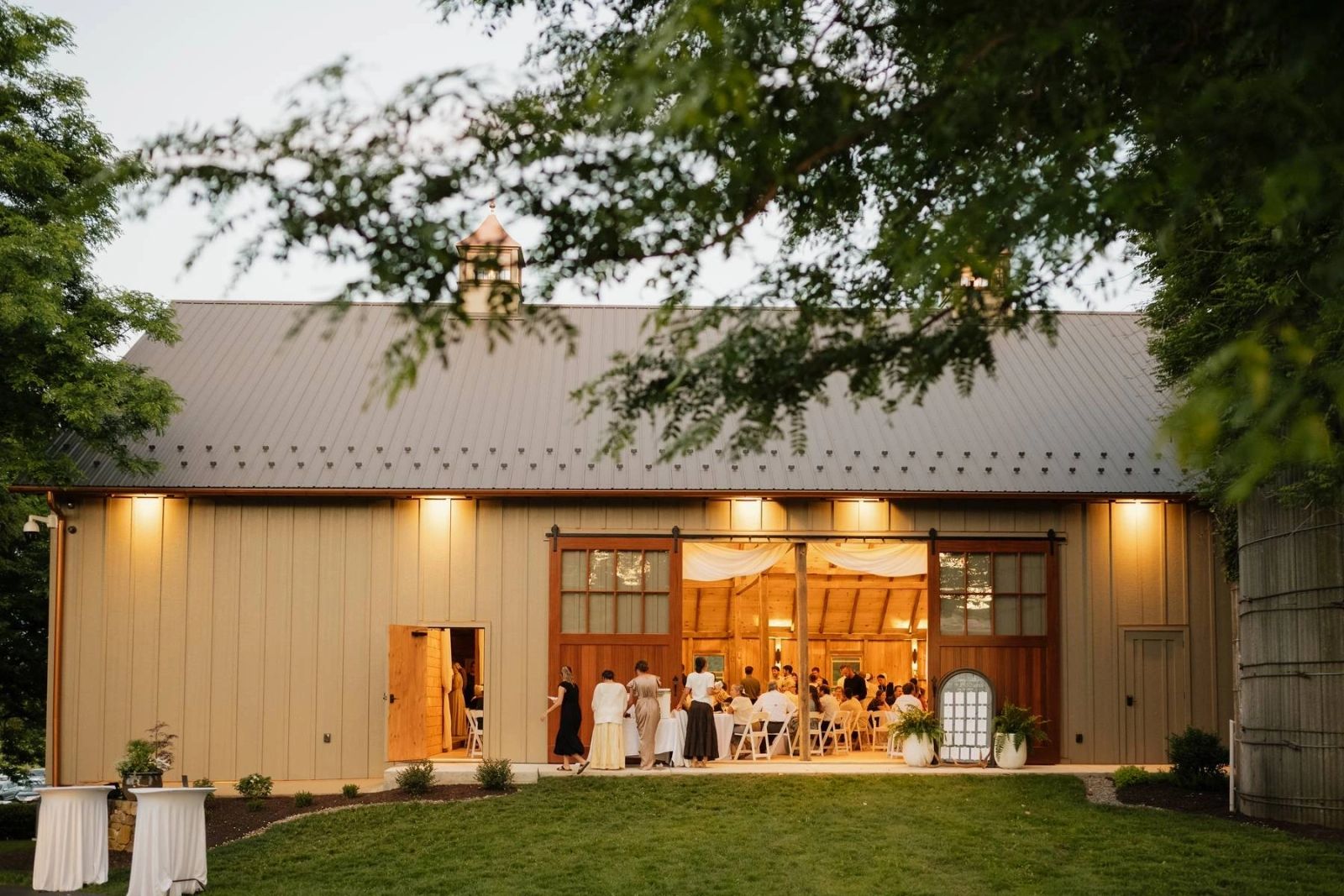 Koin-O-Nia Place event barn glowing at dusk with open doors and guests inside