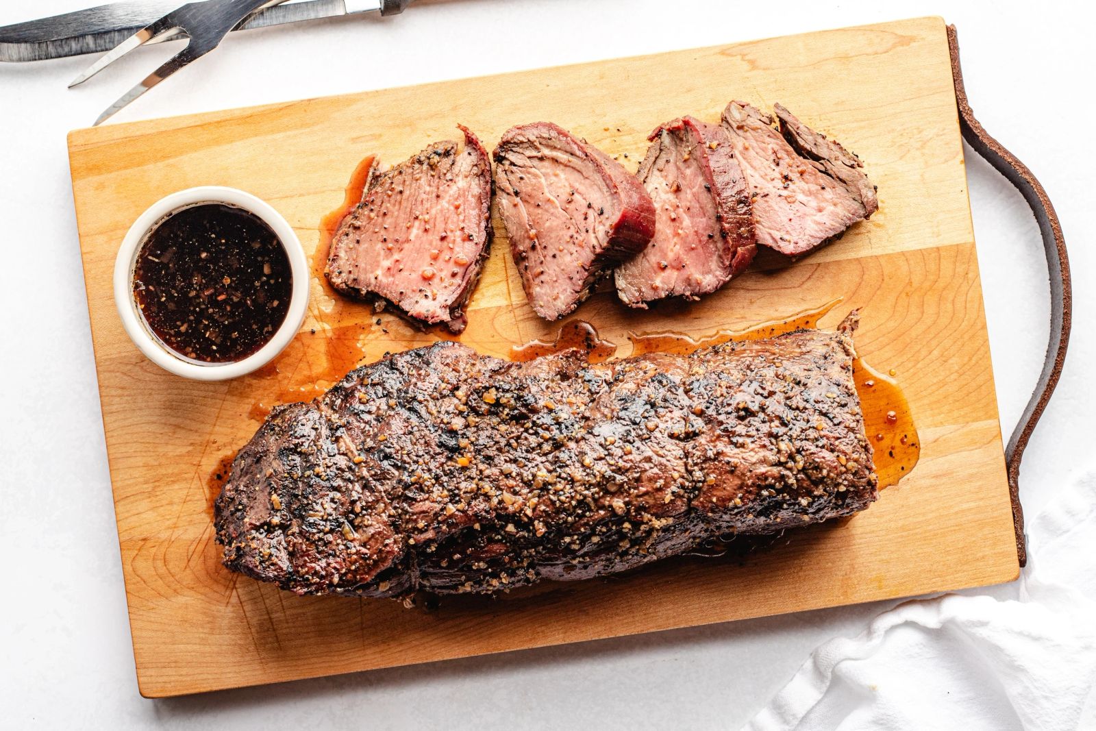 Sliced pepper-crusted steak with sauce on a wooden board, catered wedding entrée